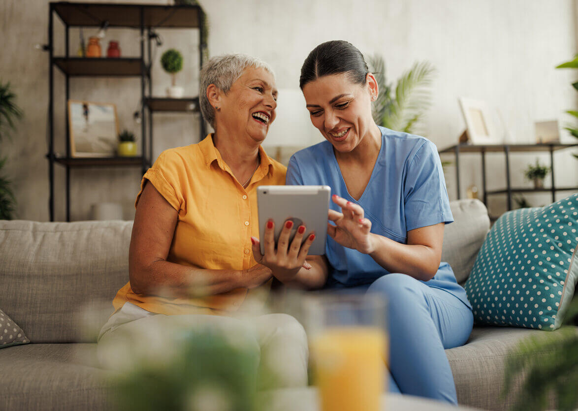 Woman wearing scrubs helping older woman on ipad