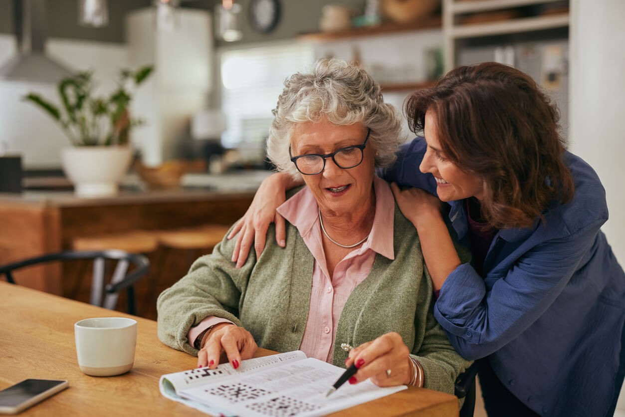 Senior woman working on a crossword puzzle in newspaper with adult daughter helping.